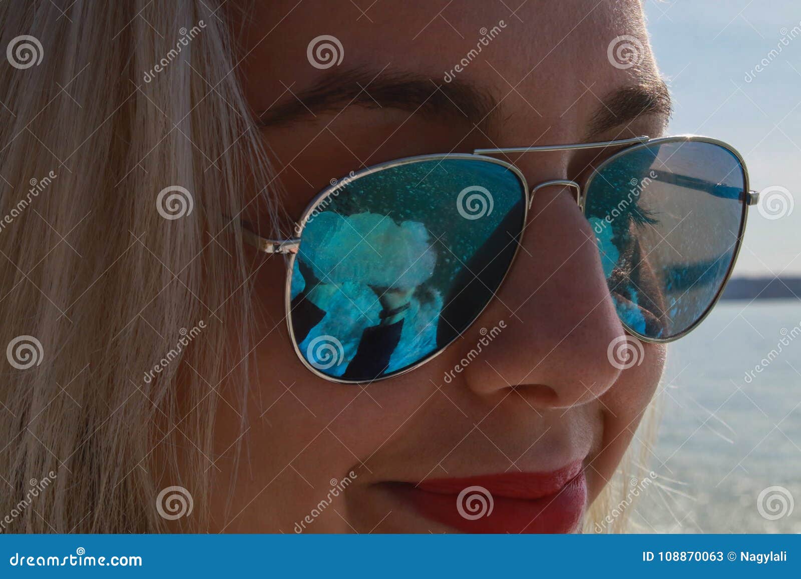 A Blonde Woman Smiles In A Pair Of Blue Sunglasses Stock