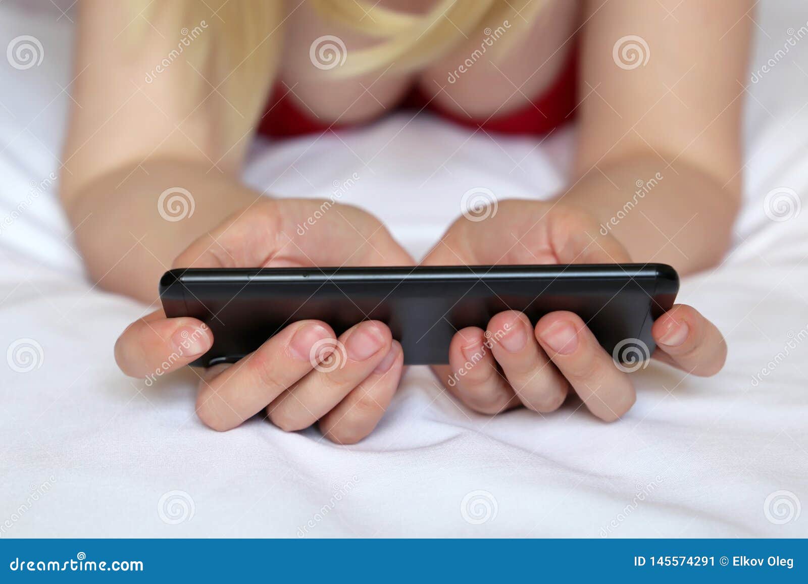 Blonde Woman Watching Video on Smartphone, Girl in Negligee Lying on the Bed Stock Image picture