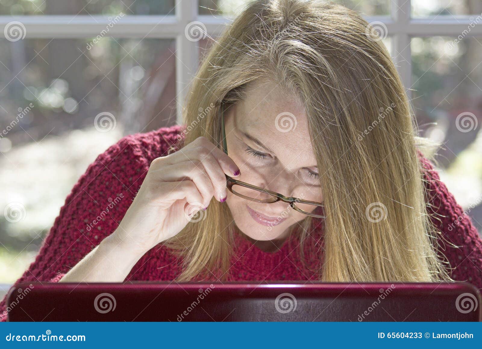 Blonder weiblicher Fokus auf Computer. Blonde Frau mit Augengläsern in der Hand konzentrierte sich auf Computer