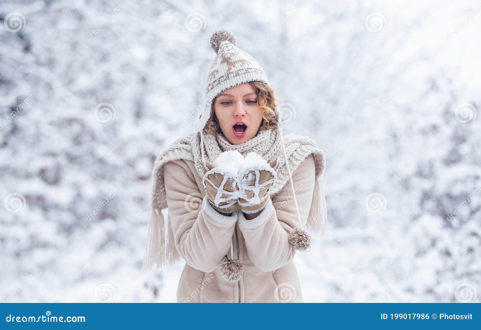 Beautiful girl in fashionable winter clothes blows snow from the