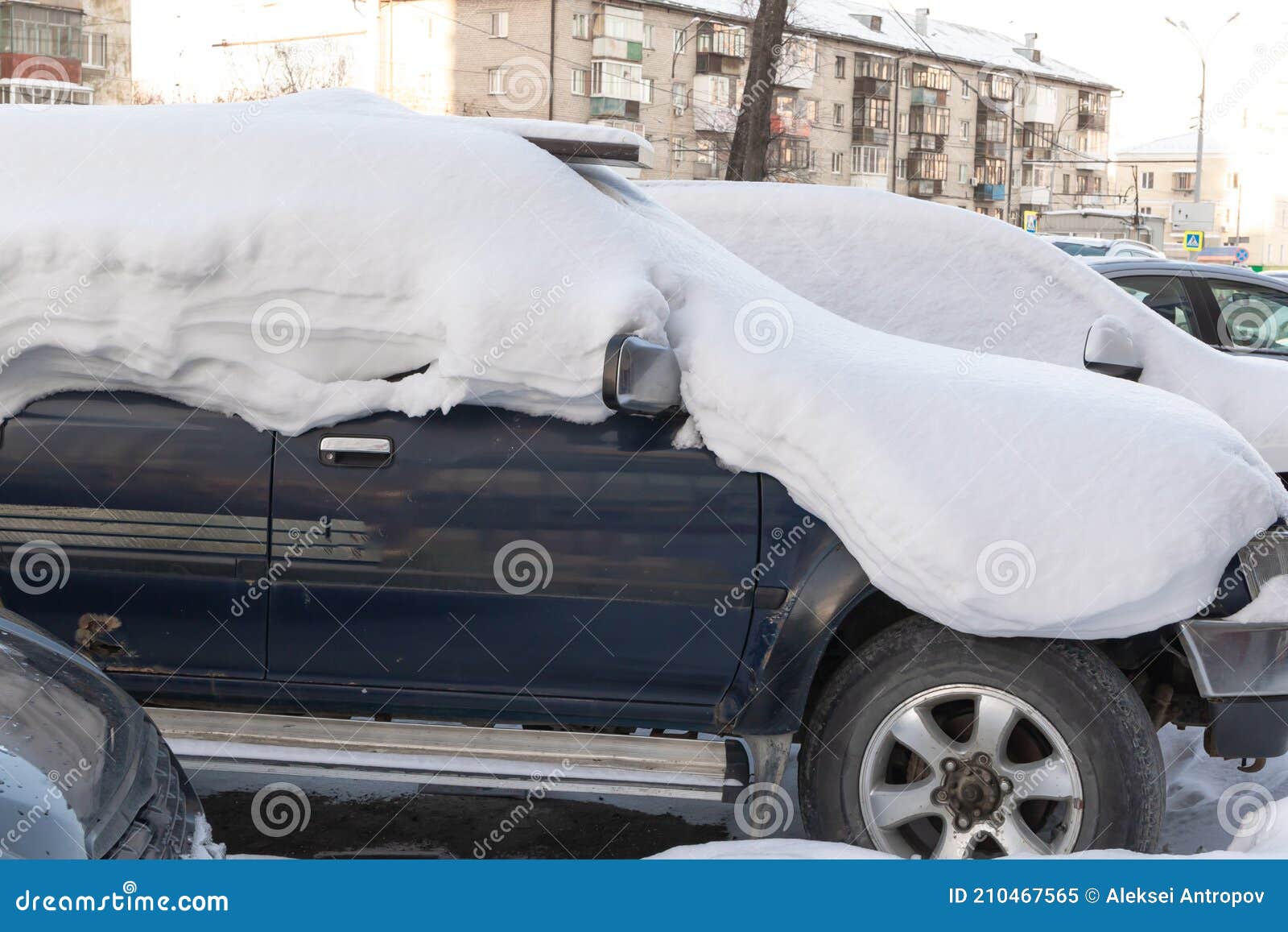 blue abandoned broken rusty car suv parked by the road under a large layer of snow on a cold winter day