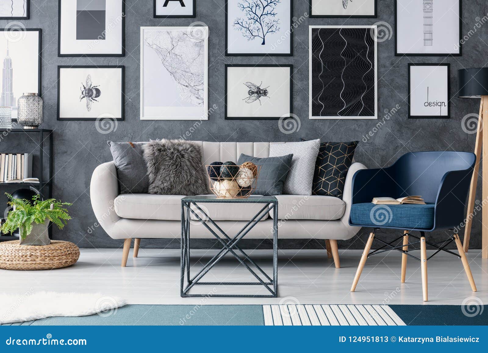 blue armchair next to sofa and table in living room interior with posters and plant on pouf. real photo
