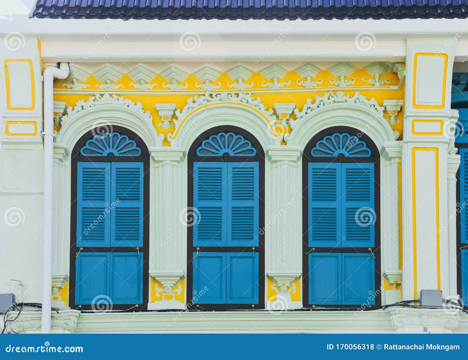blue color wooden arched window on green and yellow cement wall in chino portuguese style at phuket old town, thailand