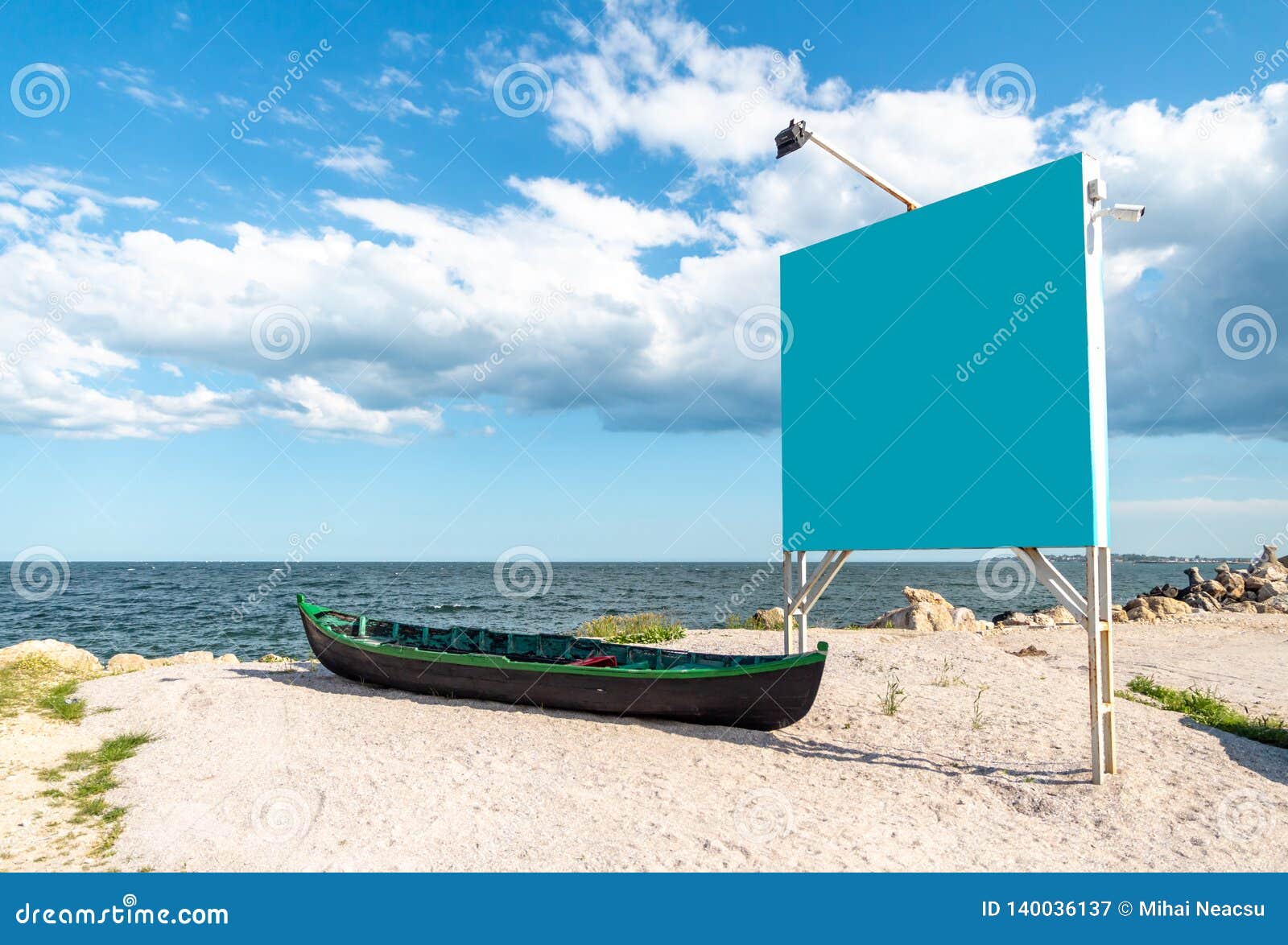 blue empty billboard next to a local, wooden fishing boat, on the sand, at shore of the black sea marea neagra, romanian coast.