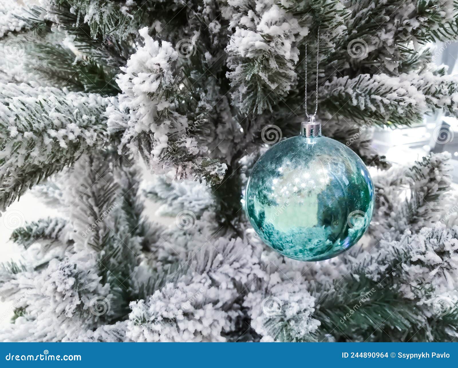 A Blue Glass Ball on a Snowcovered Christmas Tree. Artificial