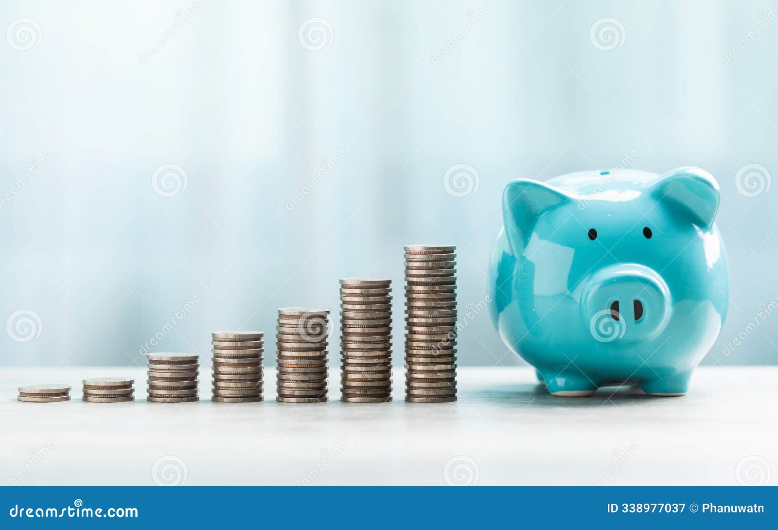 a blue piggy bank and stack of coins are neatly arranged on a table against a bright white background. the image represents the