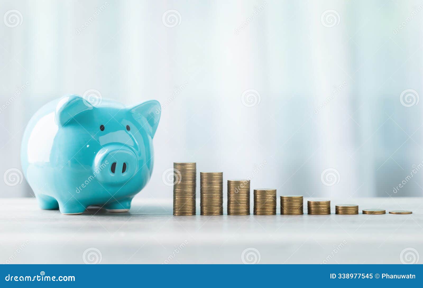 blue piggy bank and stack of coins are neatly arranged on a table against a bright white background. the image represents the