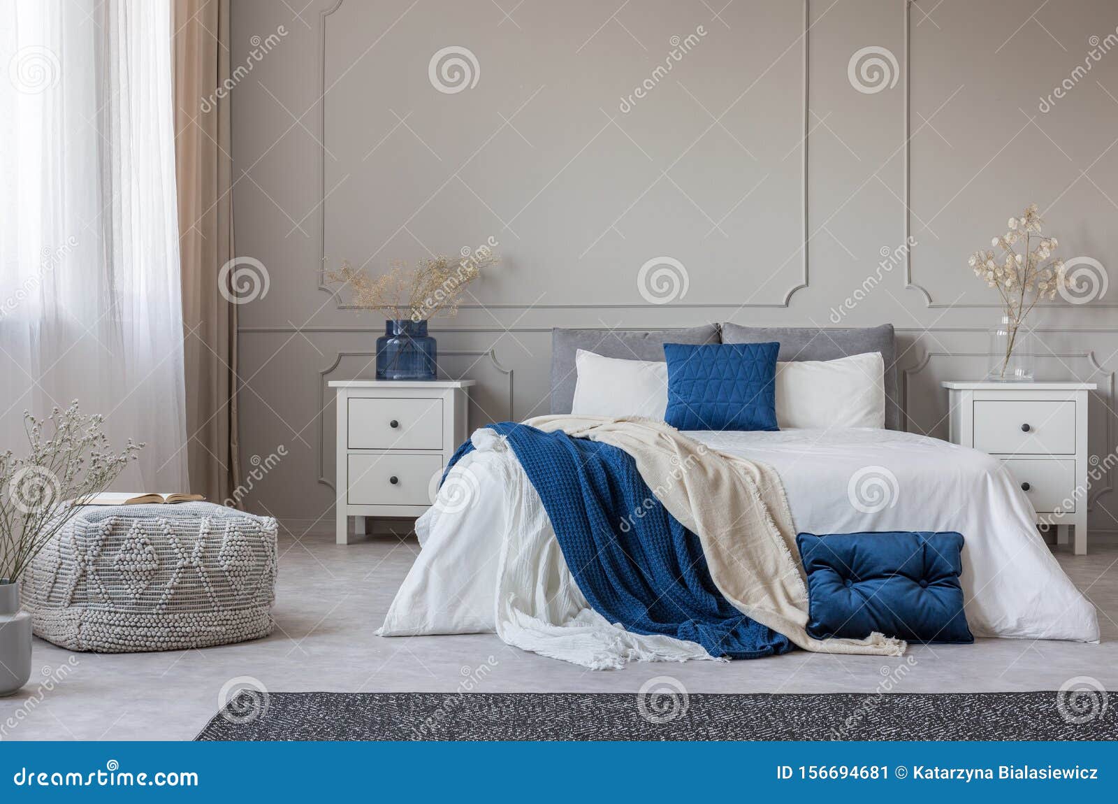 blue pillow and blanket on white bed in spacious bedroom interior, copy space on empty grey wall