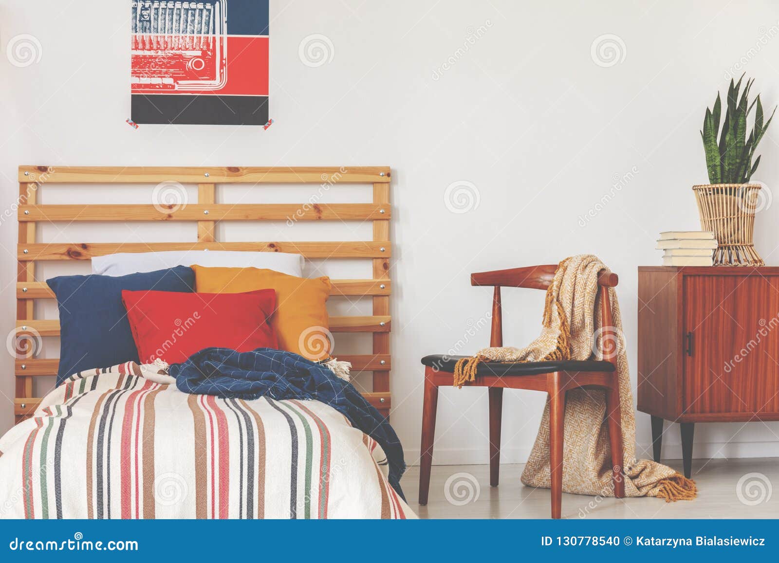 blue, red and orange pillows on single bed with stripped duvet and wooden headboard in oldschool bedroom interior, real photo