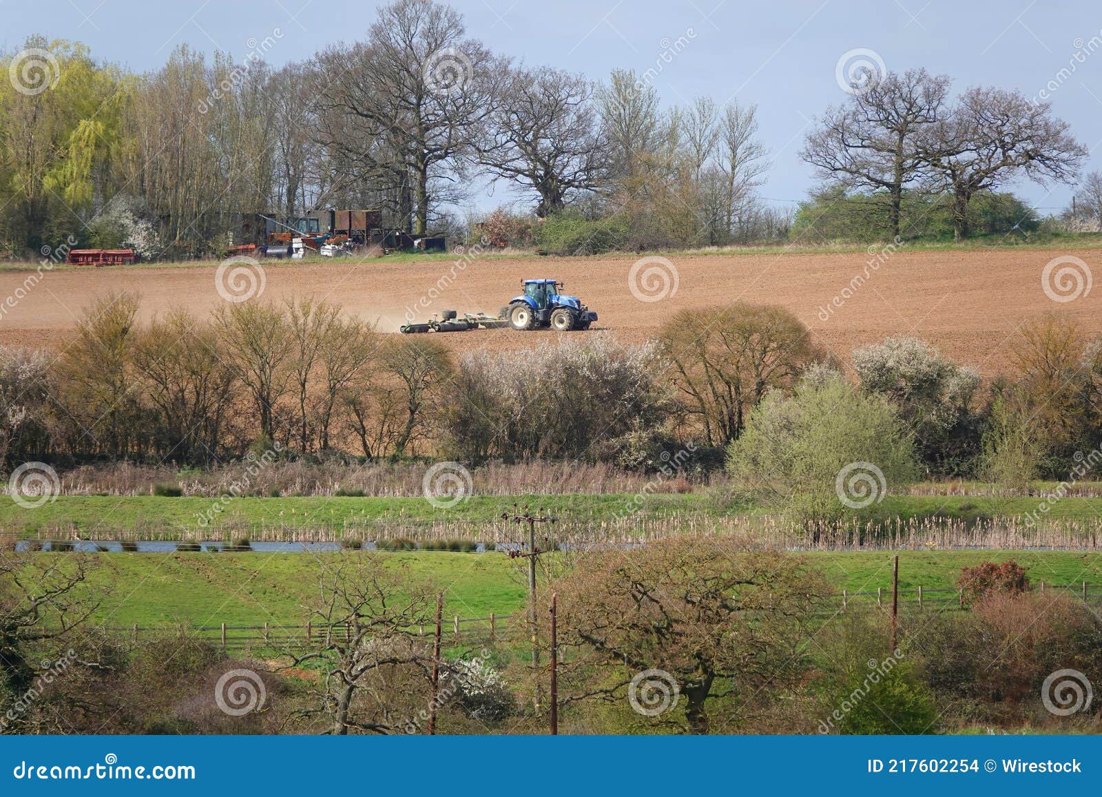 Blue Tractor Smoothing the Ground in a Farm with Trees and Grass