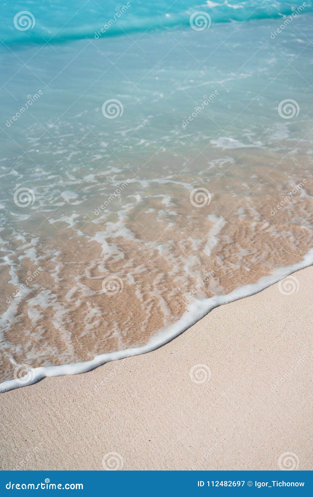 blue transparent ocean wave rolling to sandy beach with azure water. white wave foam in front