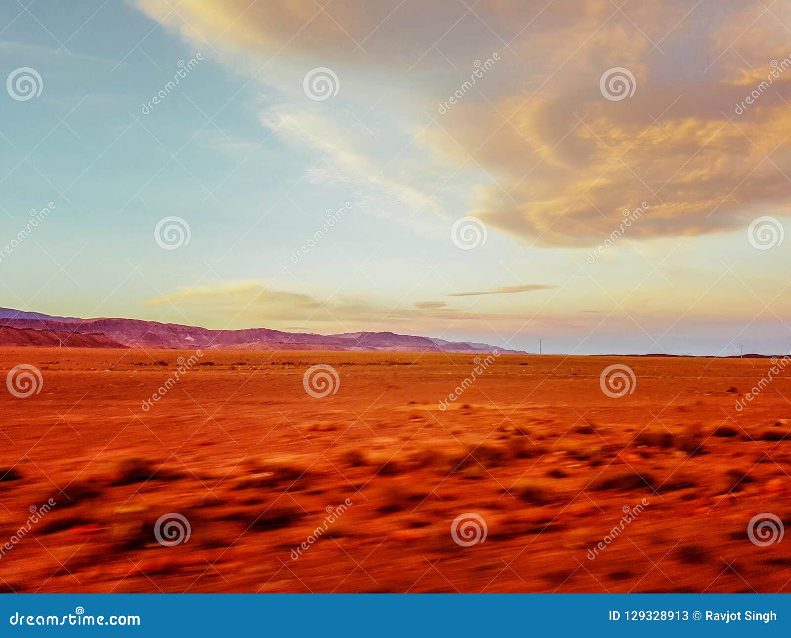 a blurred, shaky view of an empty desert sand ground landscape with cloudy sky, clicked while travelling in car to give motion blu