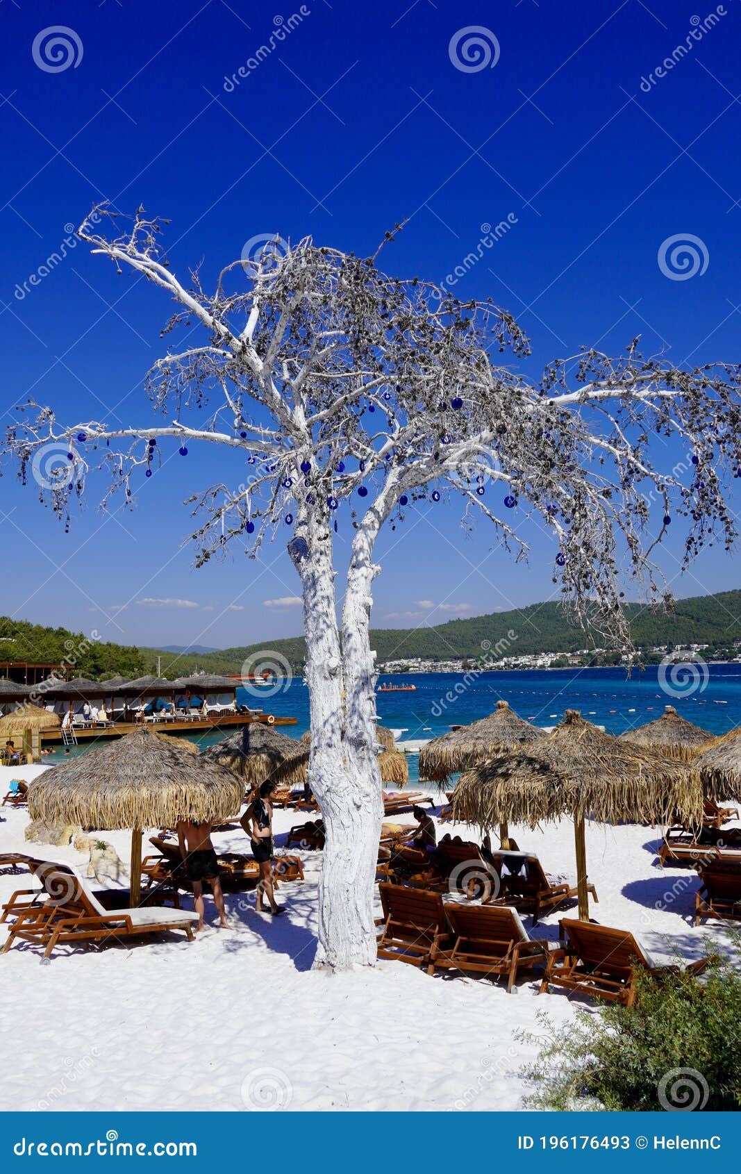 bodrum, turkey - august 2020: lujo`s snow white beach with baboon umbrellas, wooden sunbeds, emerald colored aegean sea
