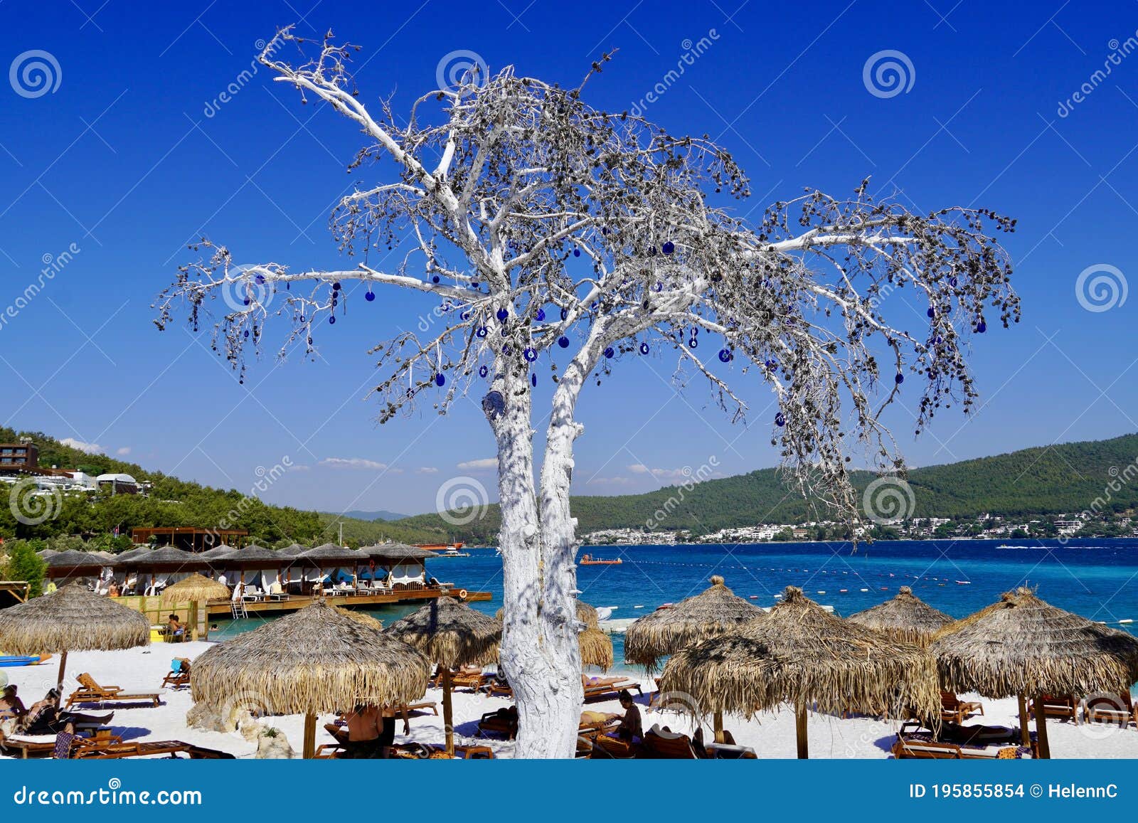 bodrum, turkey - august 2020: lujo`s snow white beach with baboon umbrellas, wooden sunbeds, emerald colored aegean sea