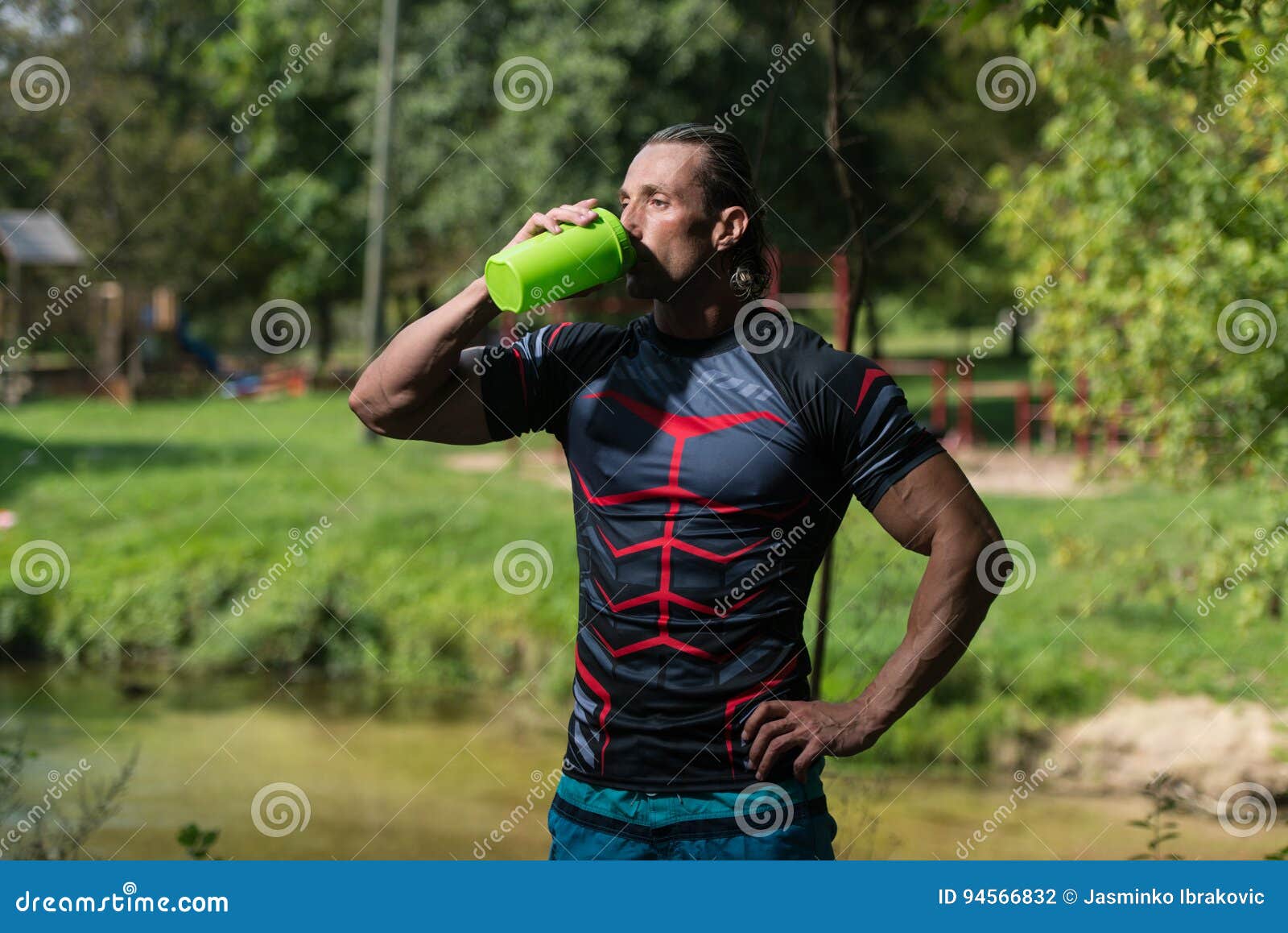 Bodybuilder Drinking Water from Shaker Outdoors in Nature Stock Photo