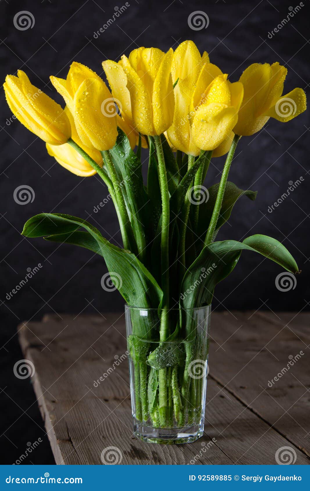 Boeket van mooie verse gele tulpen in dauw op donkere achtergrond Drie kaarsen in de vorm van appelen