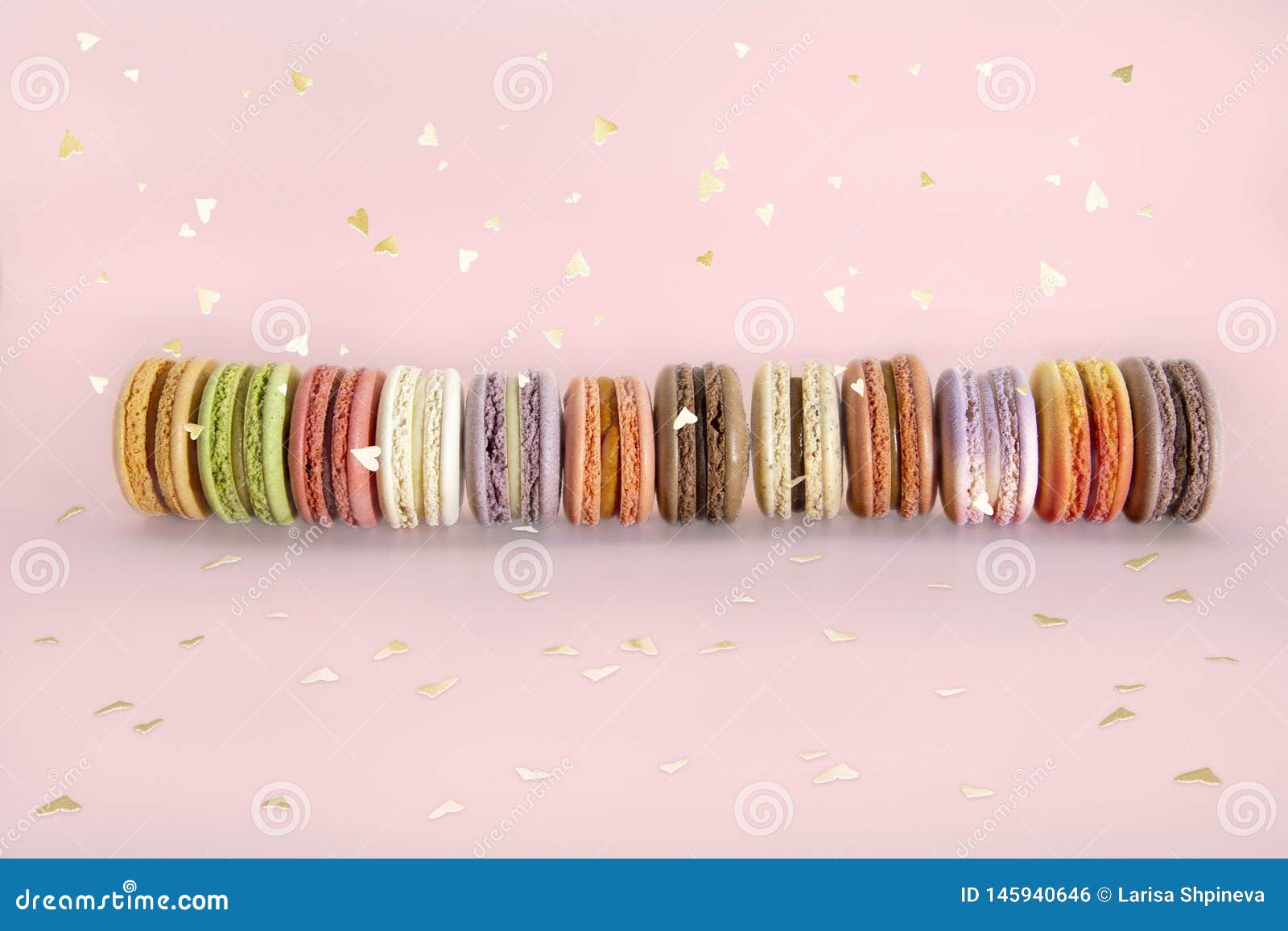 Bolinhos de am?ndoa franceses do bolo, suporte colorido doce dos macarons na fileira e confetes do ouro em claro - fundo cor-de-r. Cake french macaroons, sweet colorful macarons stand in row and gold confetti on light pink background. Birthday holiday party concept. Trendy pattern for decorative design.