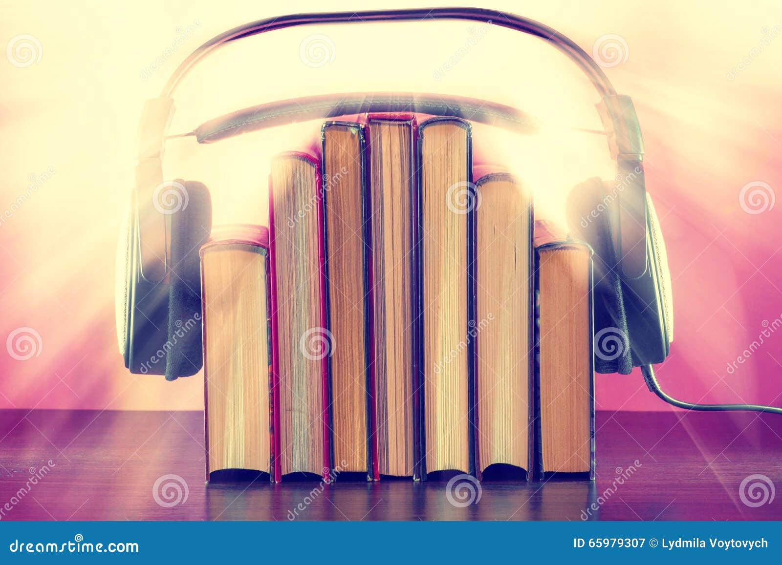 Books and headphones as an audiobook concept on a wooden table, on a pink background. The sun s rays create a joyful mood.