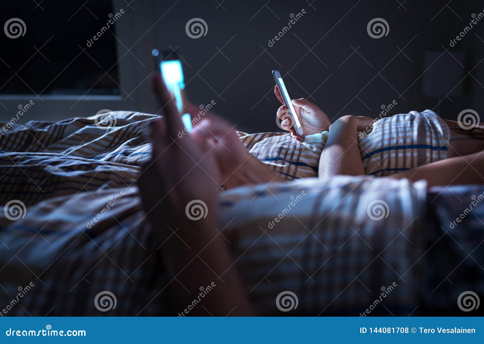 bored distant couple ignoring each other lying in bed at night while using mobile phones. smartphone addict.