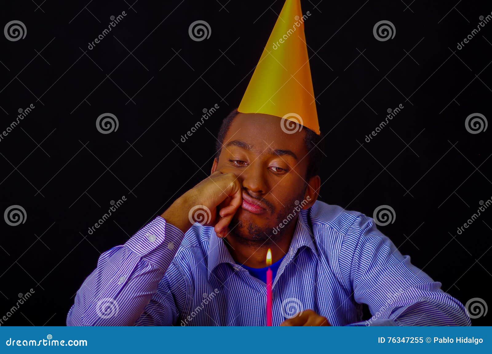 Bored Looking Man Wearing Blue Shirt and Hat Sitting by Table Holding a ...