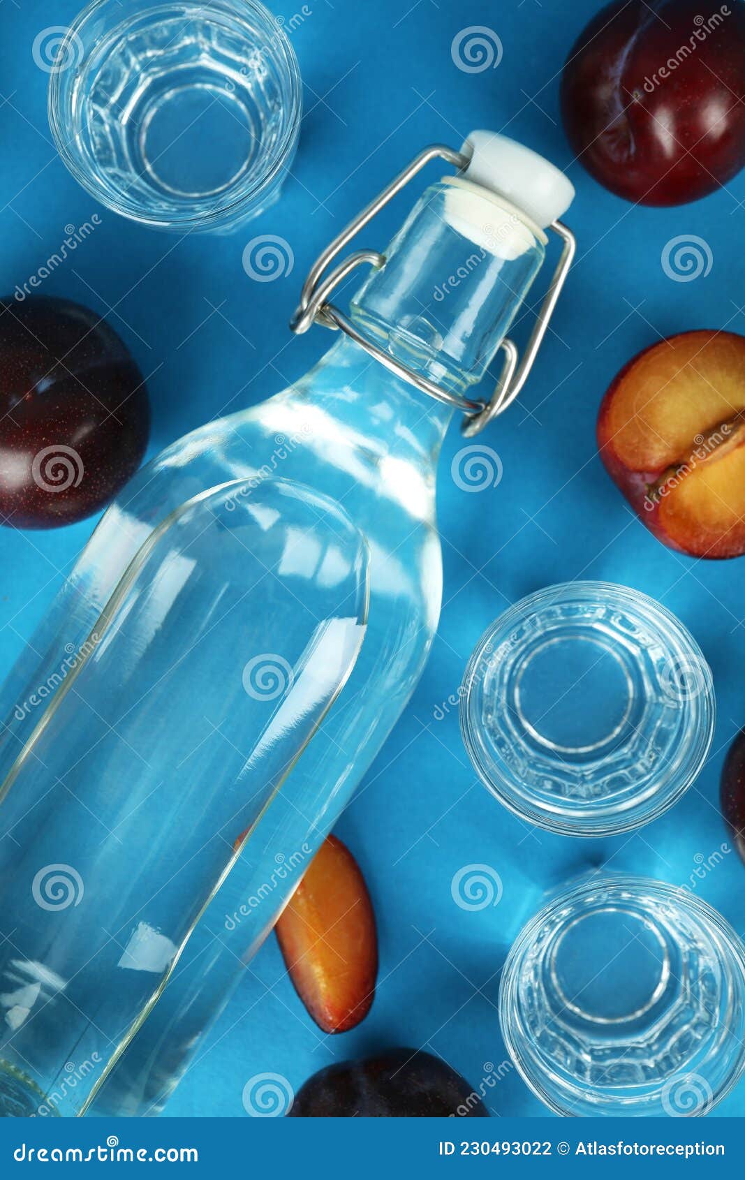 Bottle and Shots of Plum Vodka and Ingredients on Blue Background Stock