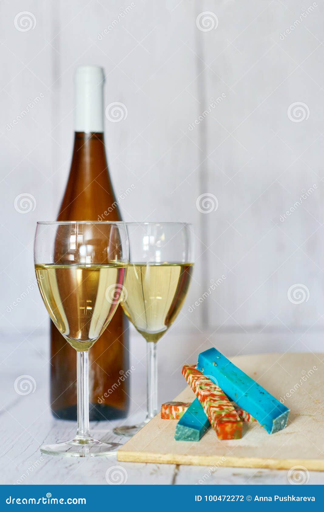 bottle and two glasses of white wine and variation of ucommon cheeses on a wooden background