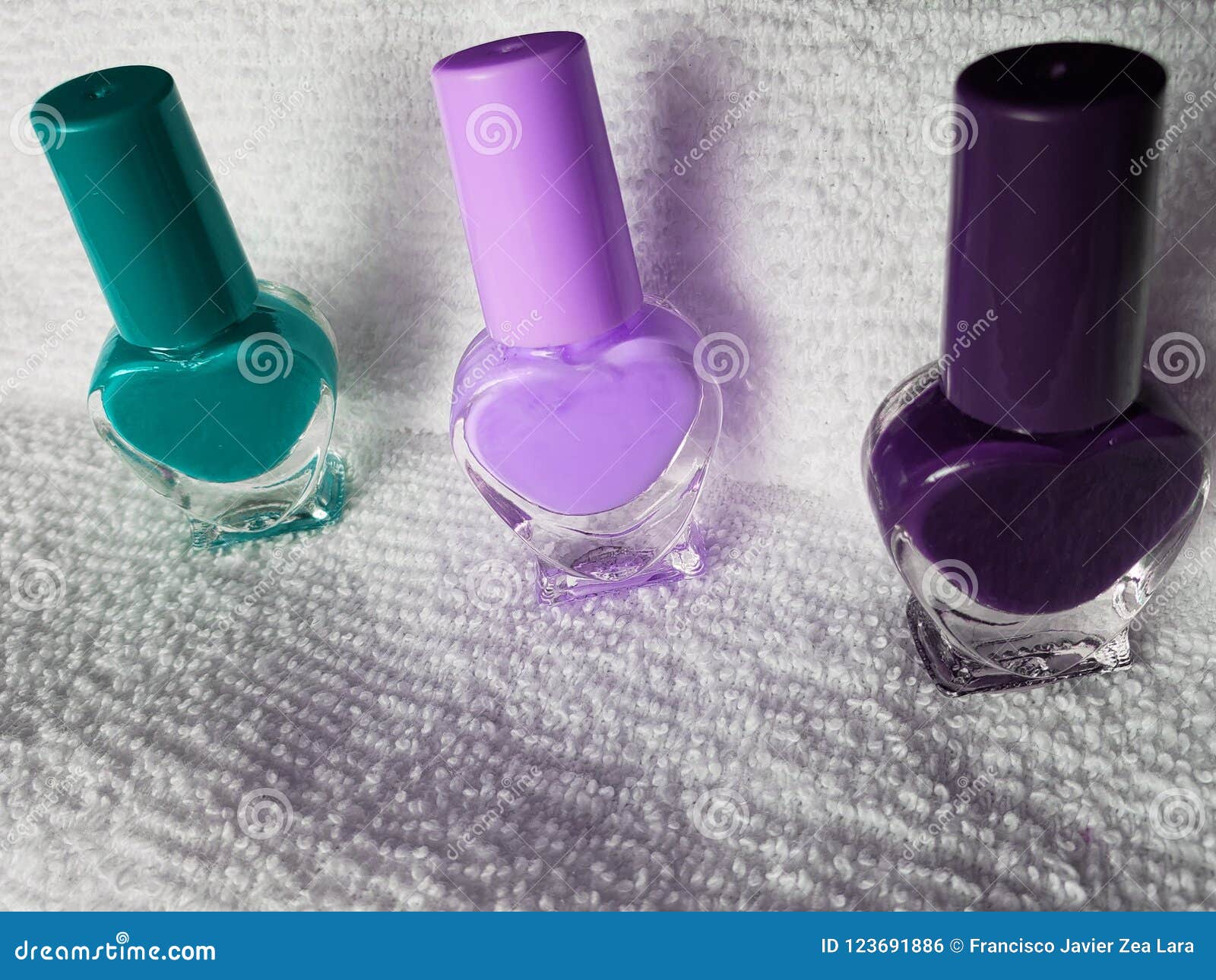 bottles with nail polish in aquamarine, pink and purple, with white background towel