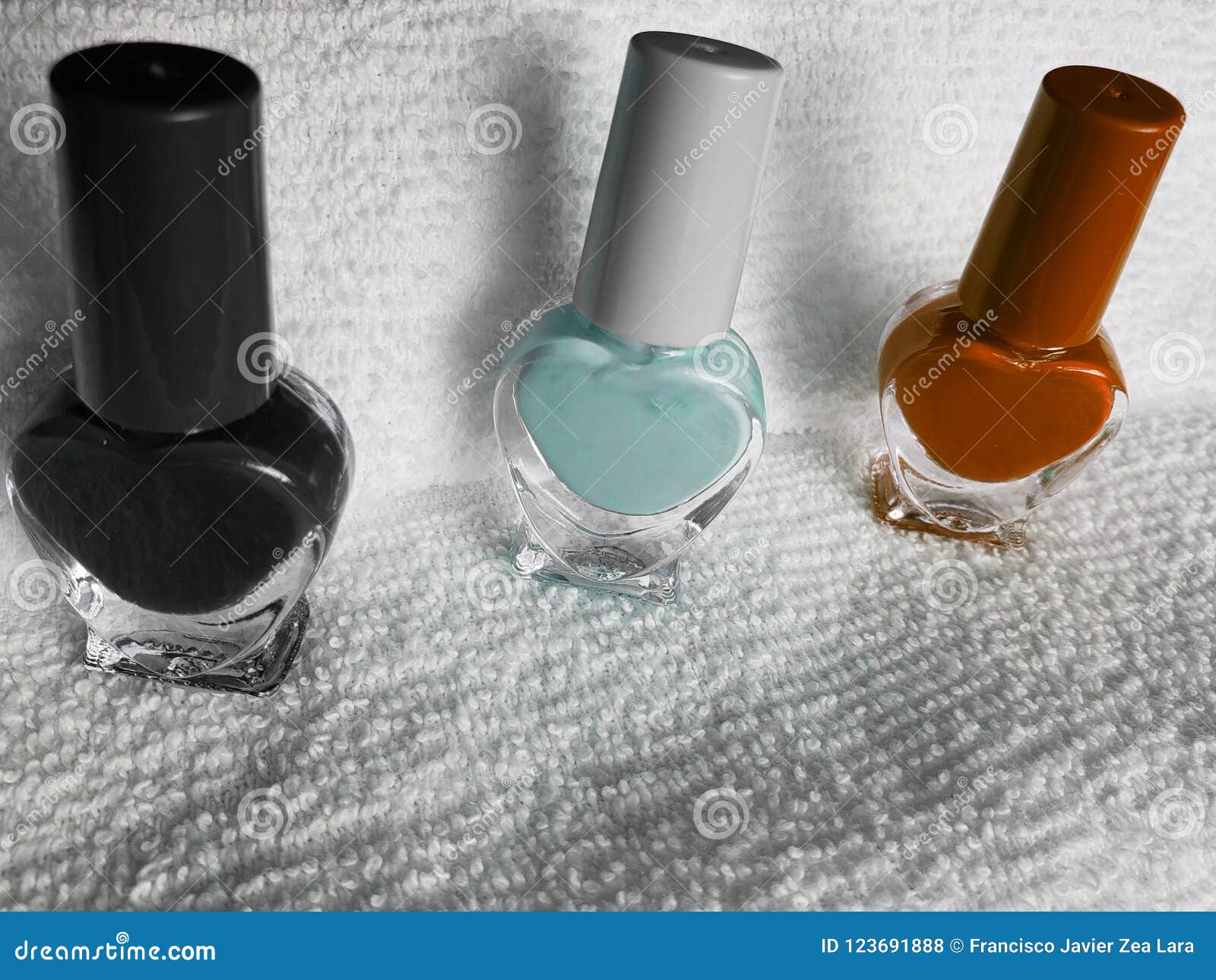 bottles with nail polish in black, light blue and orange, with white background towel