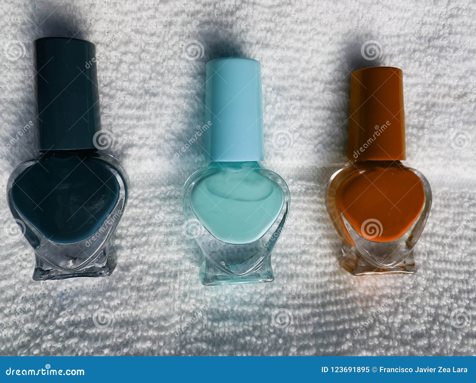bottles with nail polish in dark blue, light blue and orange, with white background towel