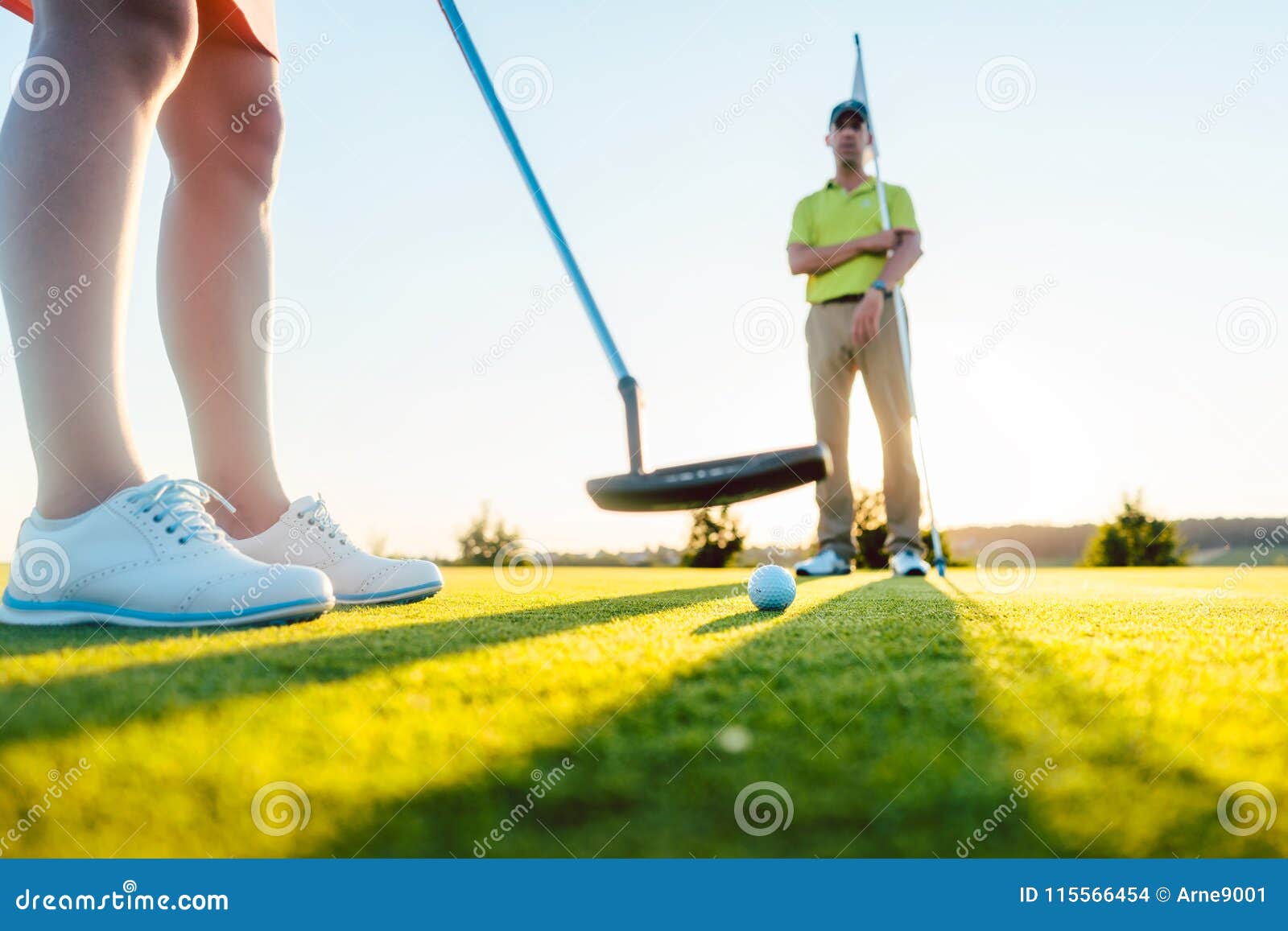 Boule de golf au foyer sélectif sous le club de putter d'un joueur féminin s'exerçant sur le putting green pendant la classe avec un professeur expérimenté