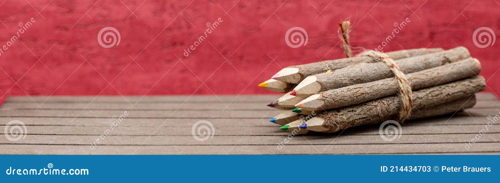 bound crayons made of untreated, real wood with real tree bark on wooden board with red background for students, artists in banner