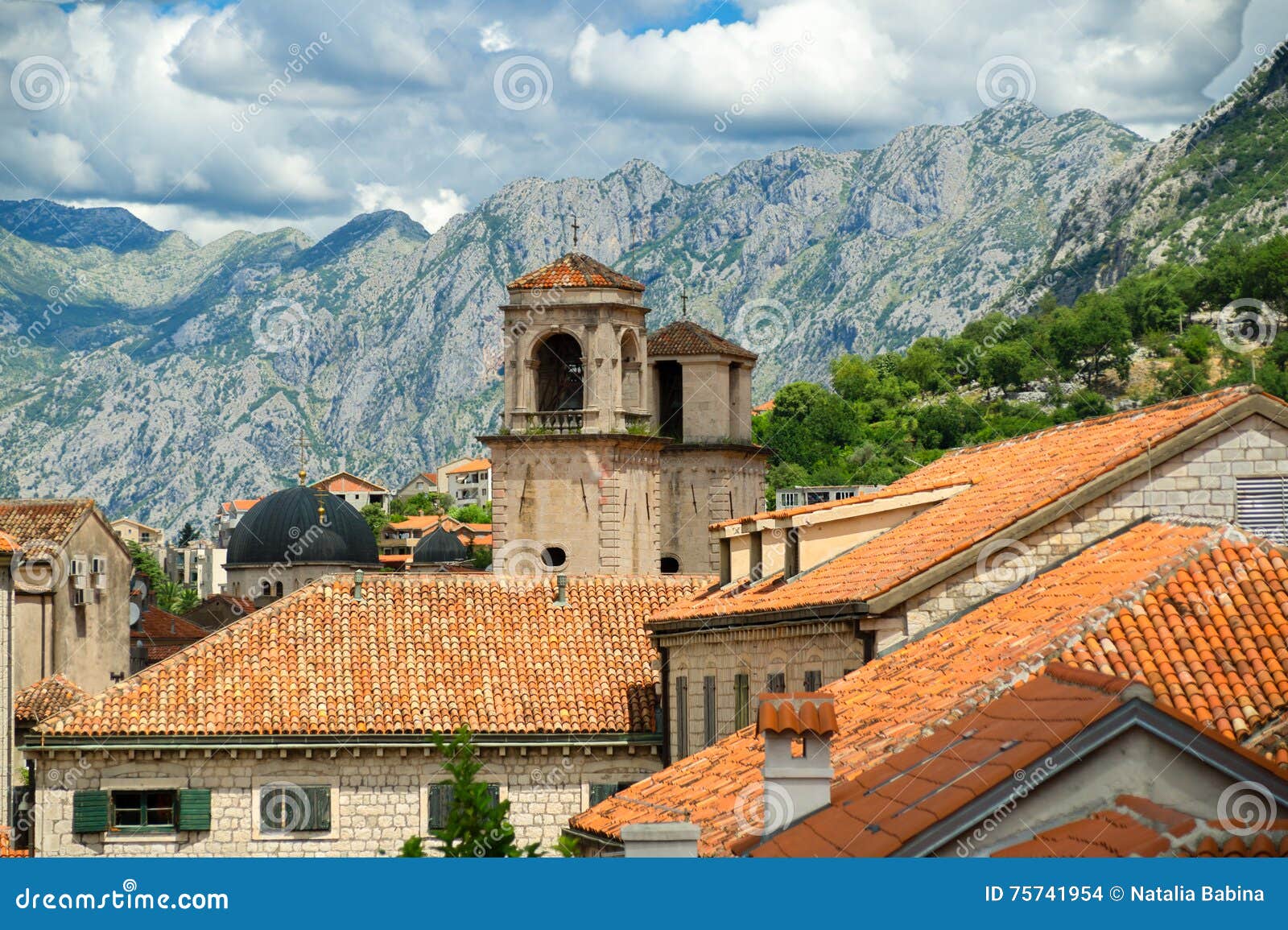 Boven rode daken van historische stad Kotor met torensst Tryphon Kathedraal, betrekken Montenegro en het landschap op achtergrond. Boven rode daken van historische stad Kotor in baai van Kotor, met torens van St Tryphon Kathedraal, Montenegro op bergachtergrond