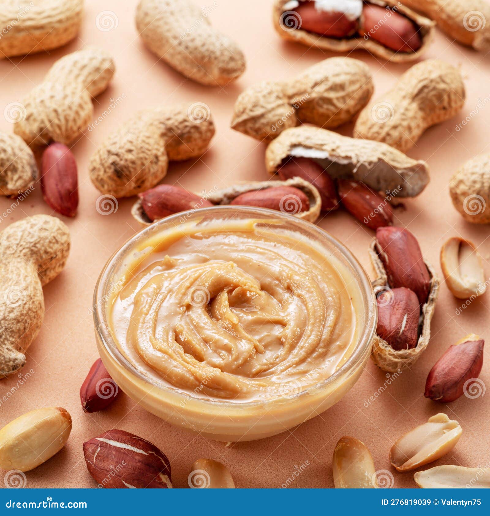 Bowl of Peanut Butter and Peanuts Around it on Beige Background. Top