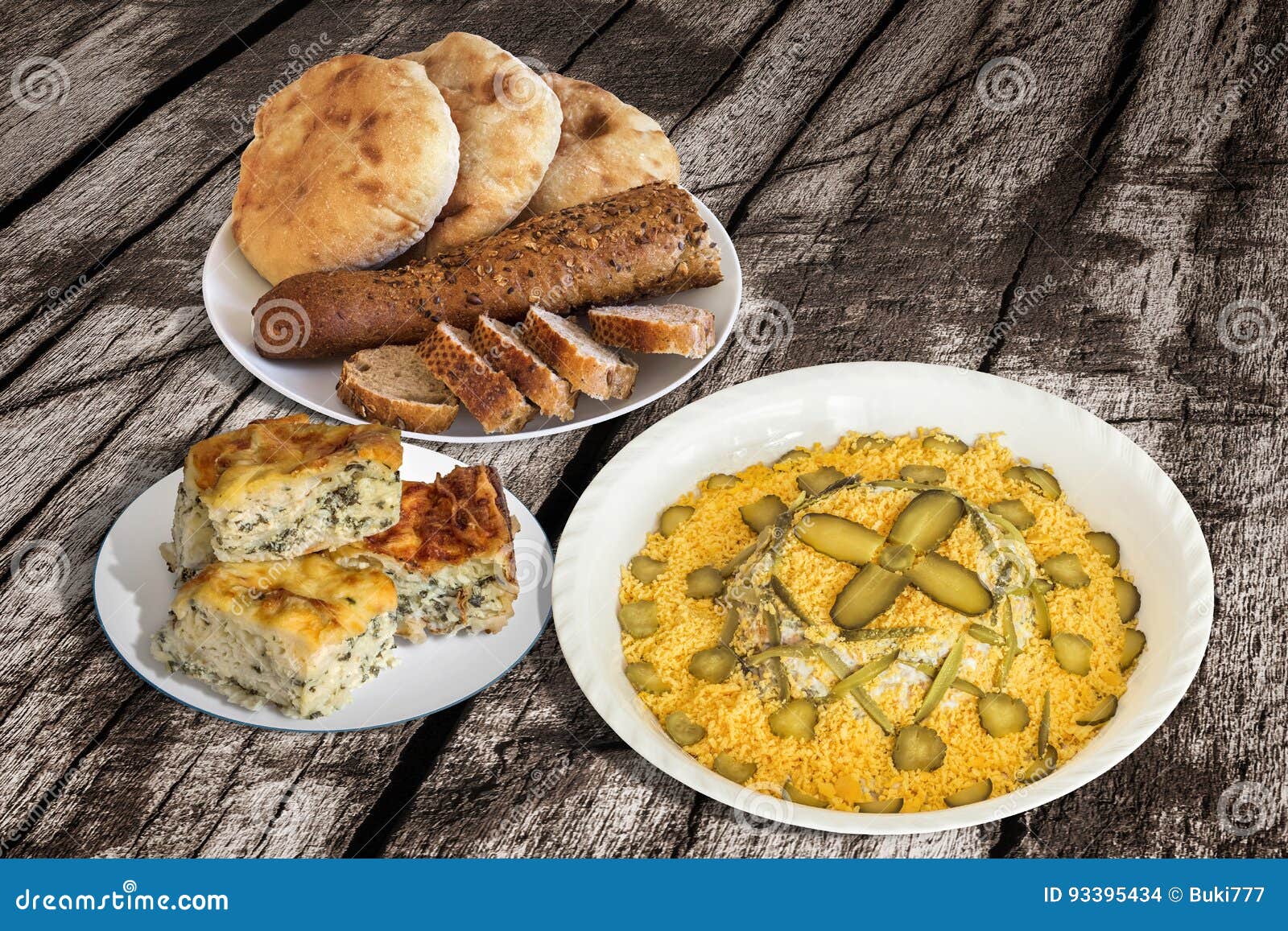 bowl of russian salad with baguette slices and pitta bread loafs with spinach cheese pie set on old wooden garden table