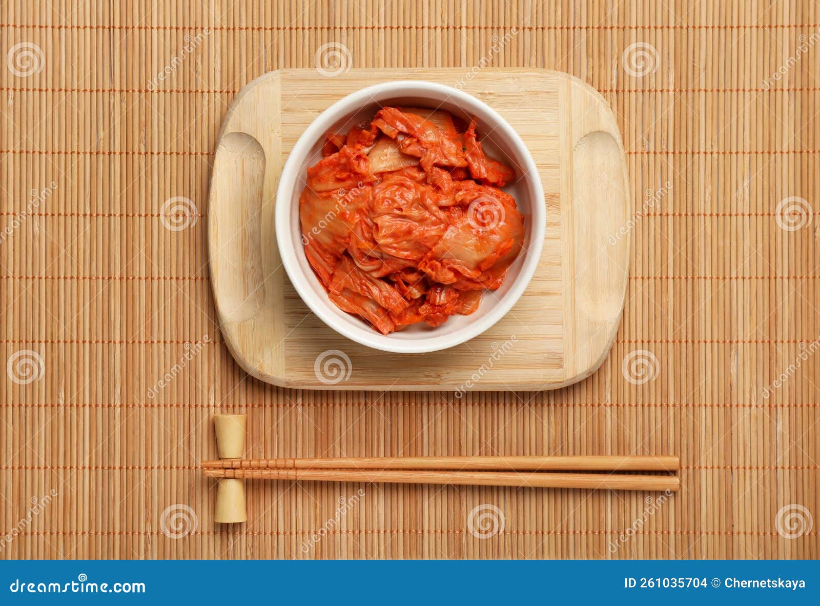 Bowl of Spicy Cabbage Kimchi and Chopsticks on Bamboo Mat, Flat Lay
