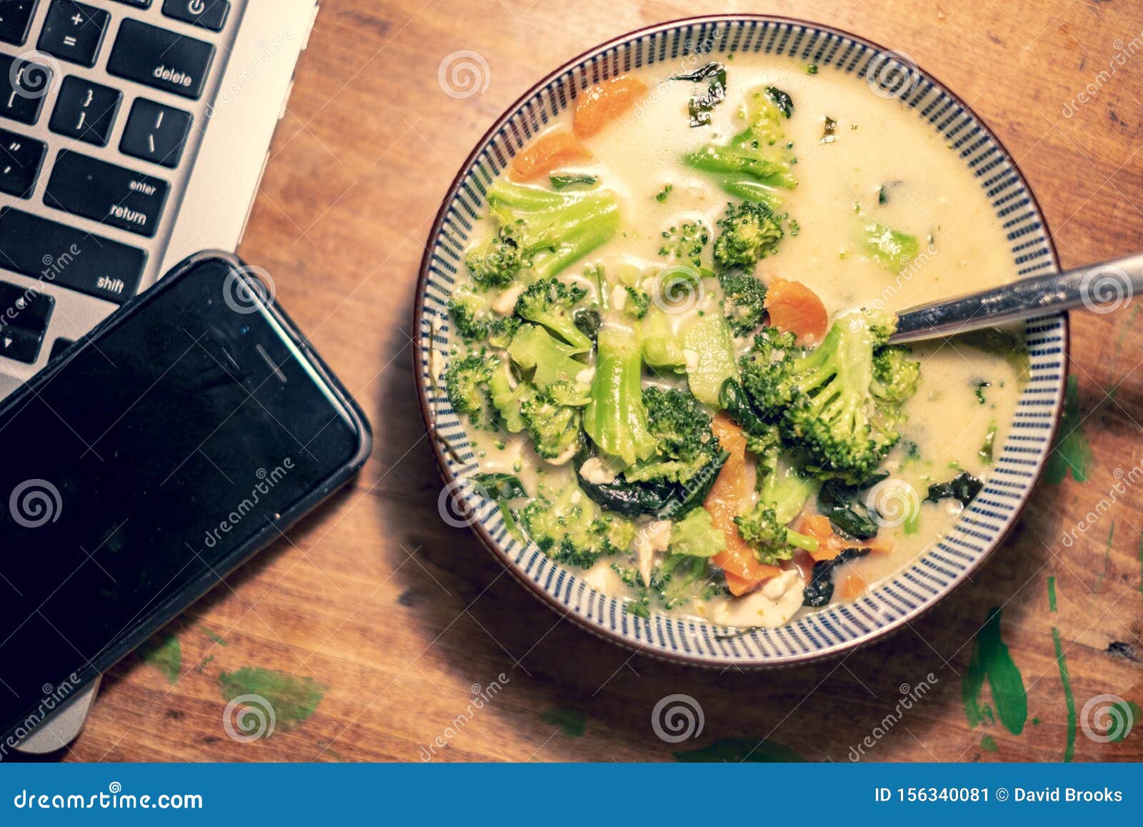 bowl of thai curry soup next to laptop and phone
