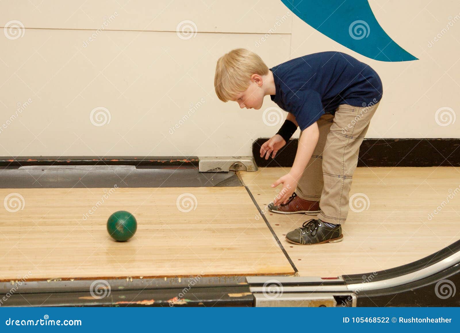 Bowling d'enfant avec la boule. Un jeune garçon blond se plie plus d'et lance la boule de bowling en bas d'une allée