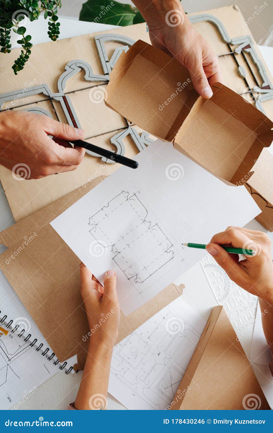 Box Makers Working Behind a Table, Discussing Schematics of a Box Stock