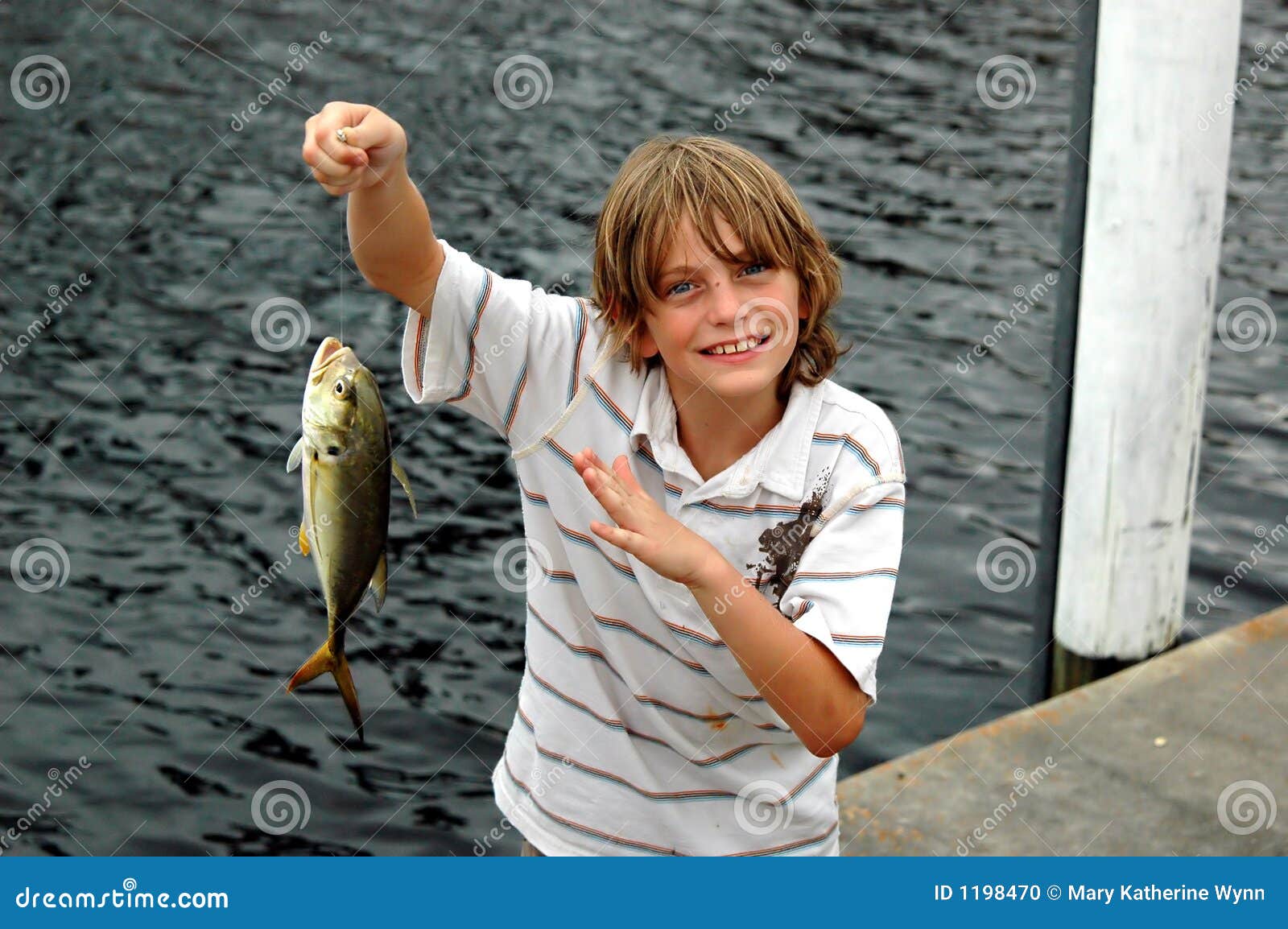 Funny happy little kid fishing on weekend. A fisherman boy stands in the  lake with a fishing rod and catches fish. Stock Photo