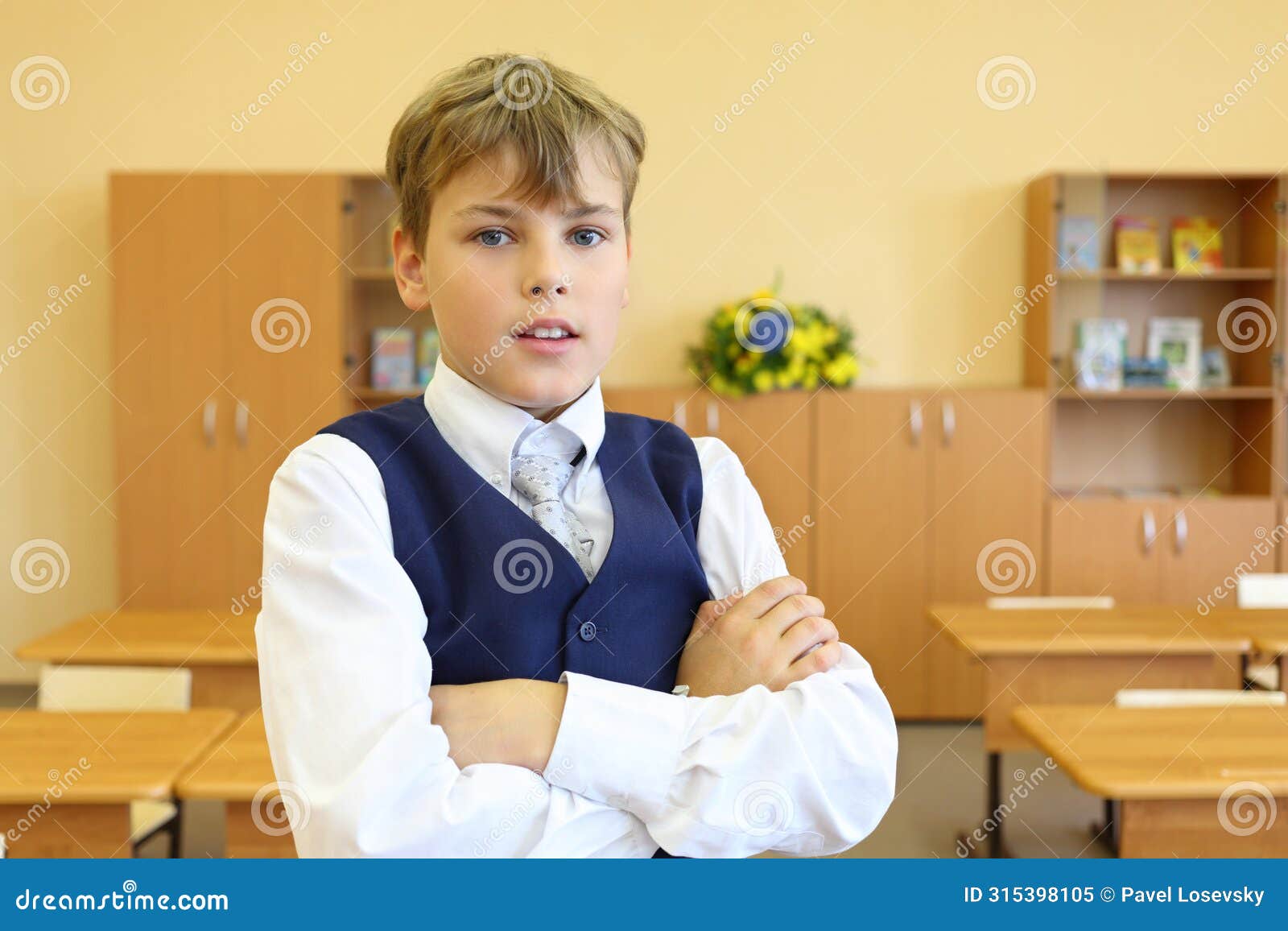 boy with crossed arms stands in empty classroom