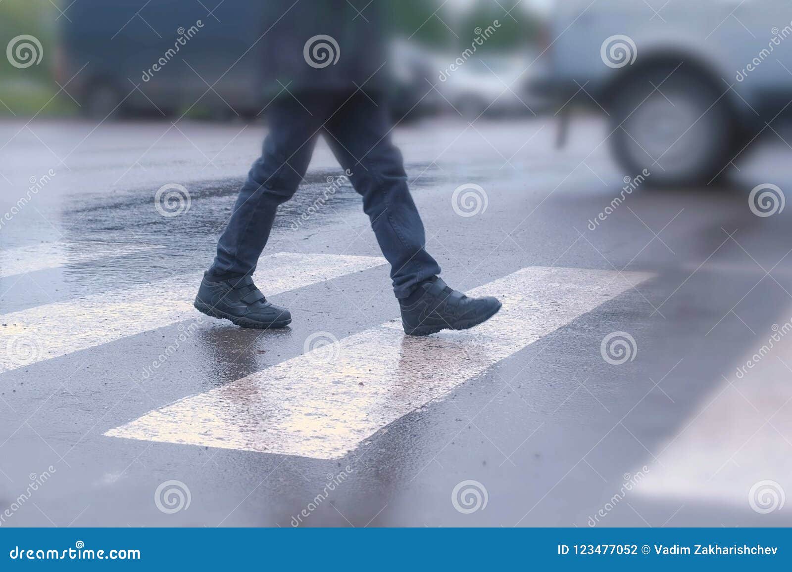 boy crosses the road at a pedestrian crossing in the rain. legs close-up.
