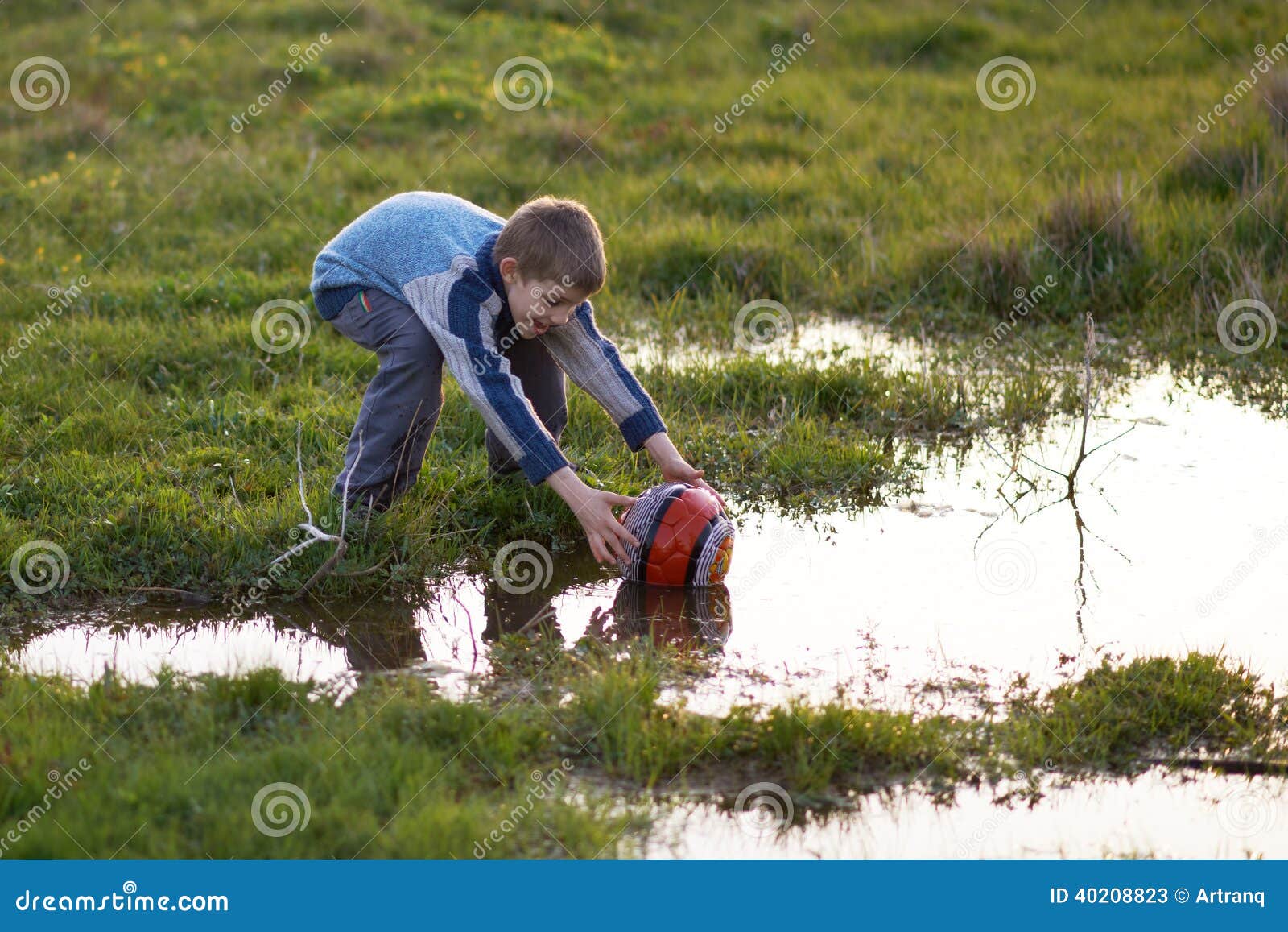 boy gets ball with puddles in the grass