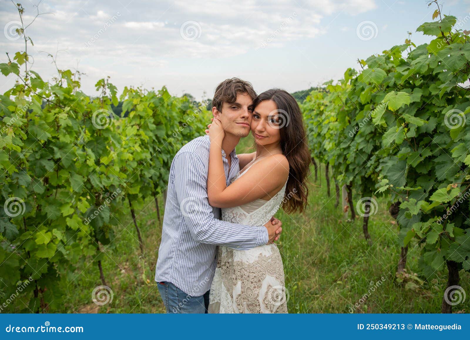 boy and girl in love look smilingly at the photographer who portrays them in the midst of the vineyards