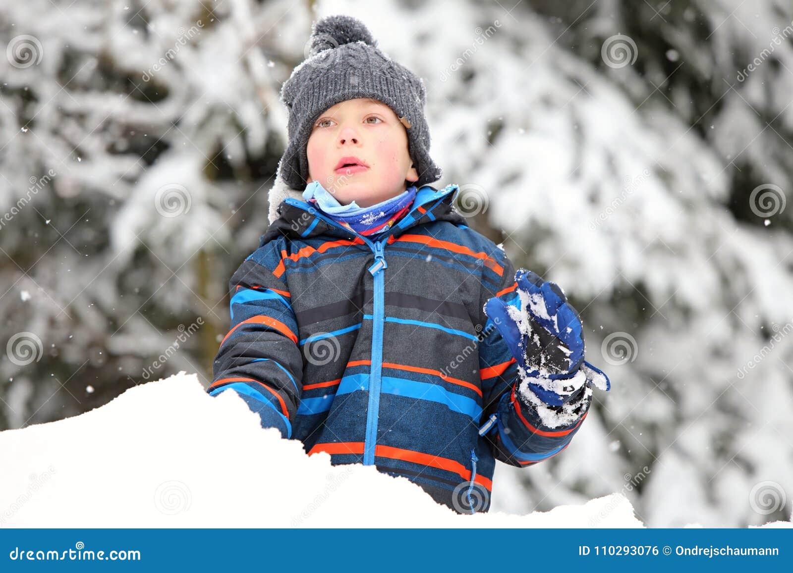 boy with gray stocking cap and color striped jacket playin on the snow pile