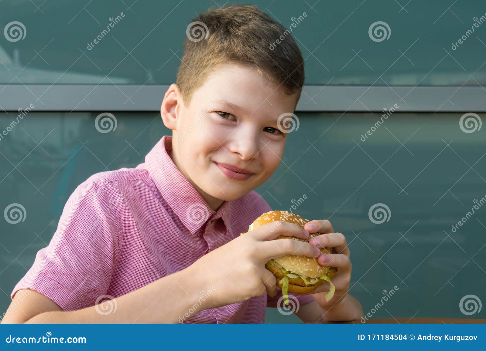 The Boy Holds a Burger in His Hands and Smiles before Eating it Stock