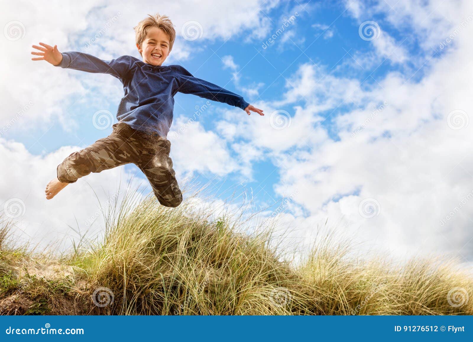 Boy Leaping and Jumping Over Sand Dunes on Beach Vacation Stock Photo
