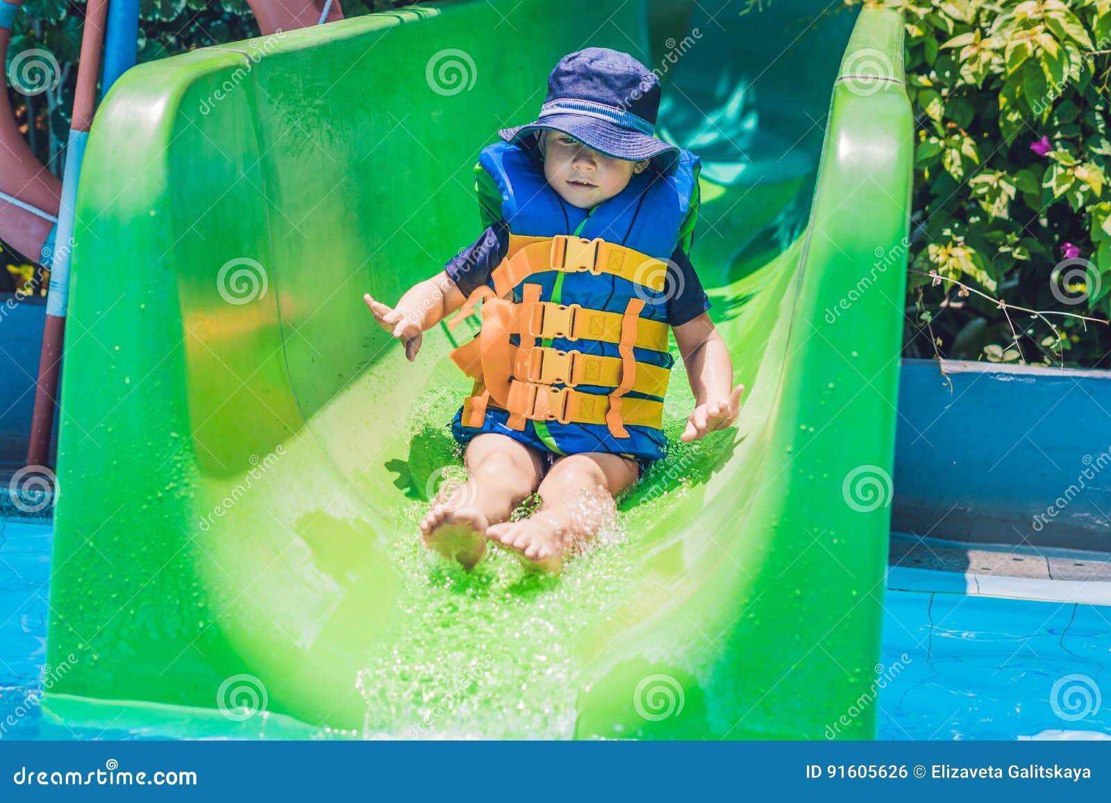 A Boy in a Life Jacket Slides Down from a Slide in a Water Park Stock