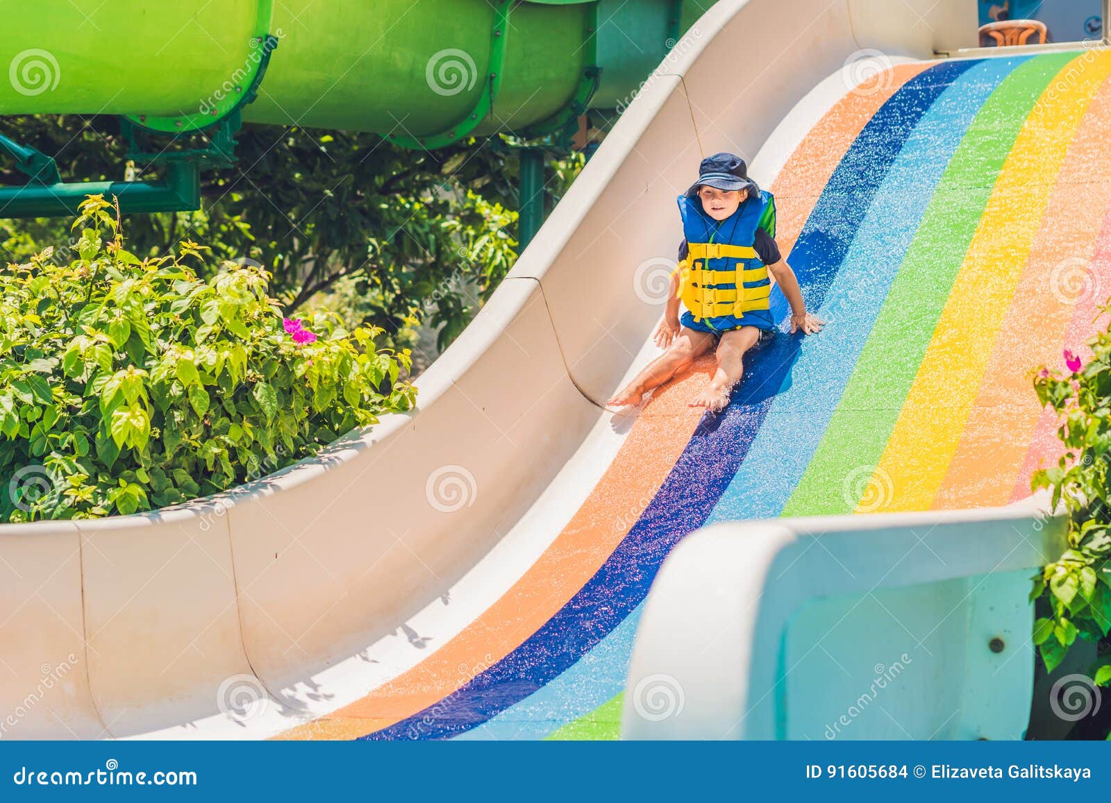 A Boy in a Life Jacket Slides Down from a Slide in a Water Park Stock