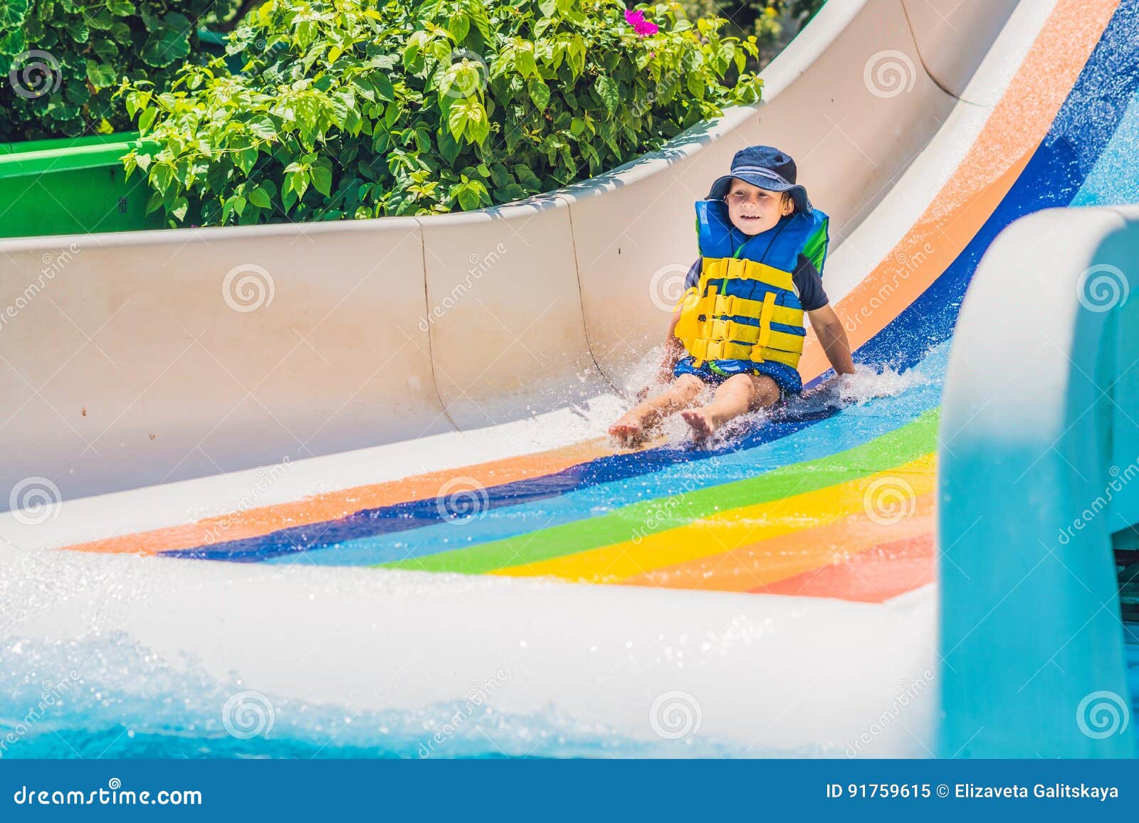 A Boy in a Life Jacket Slides Down from a Slide in a Water Park Stock