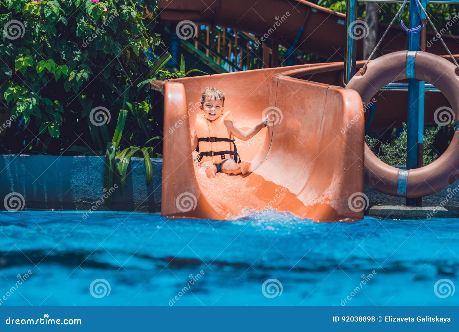 A Boy in a Life Jacket Slides Down from a Slide in a Water Park Stock